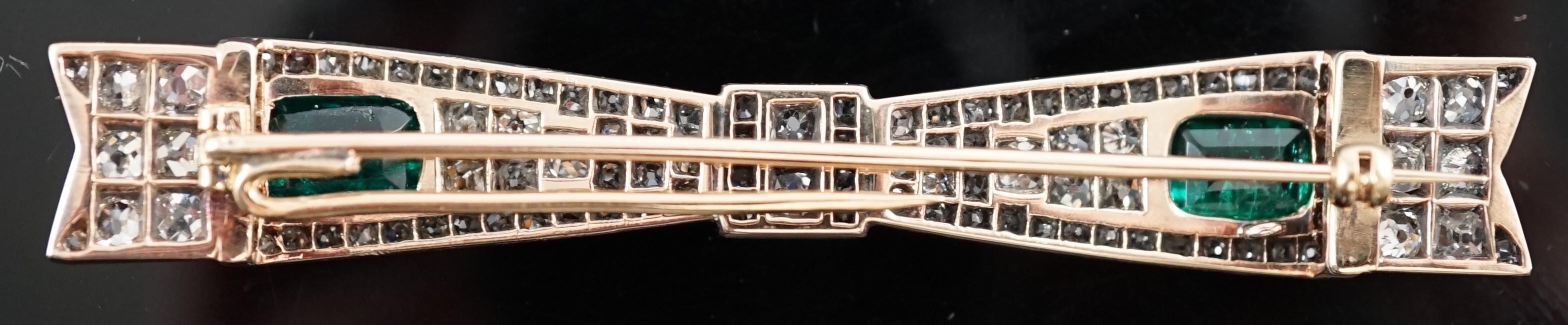 A 1920's gold and platinum, two stone emerald and graduated diamond cluster set ribbon bow bar clip brooch